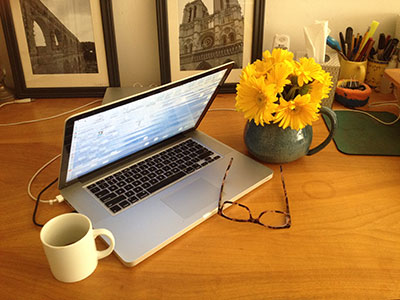 partially open laptop, flower, coffee cup, and glasses on top of a desk