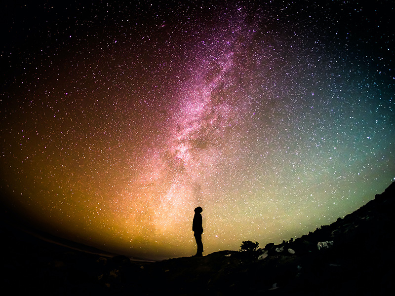 Silhouette of a person in front of a night sky full of stars and galaxies.