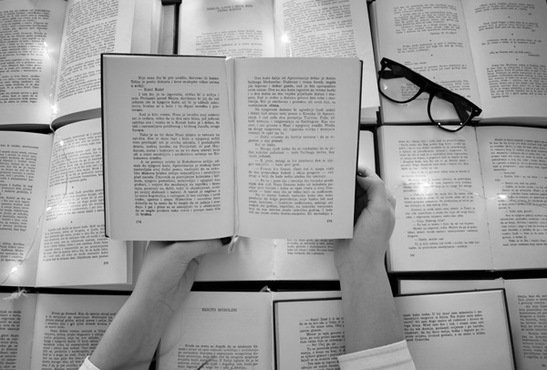 Hands holding an open book above other open books.