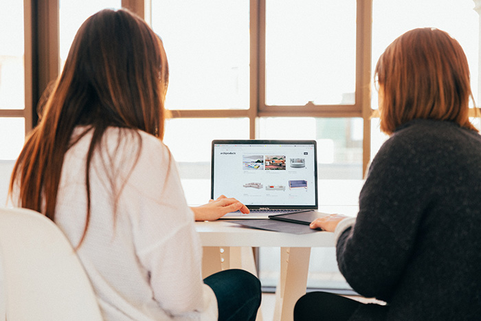 A writer working with her writing coach on a computer, both with their backs to the camera.